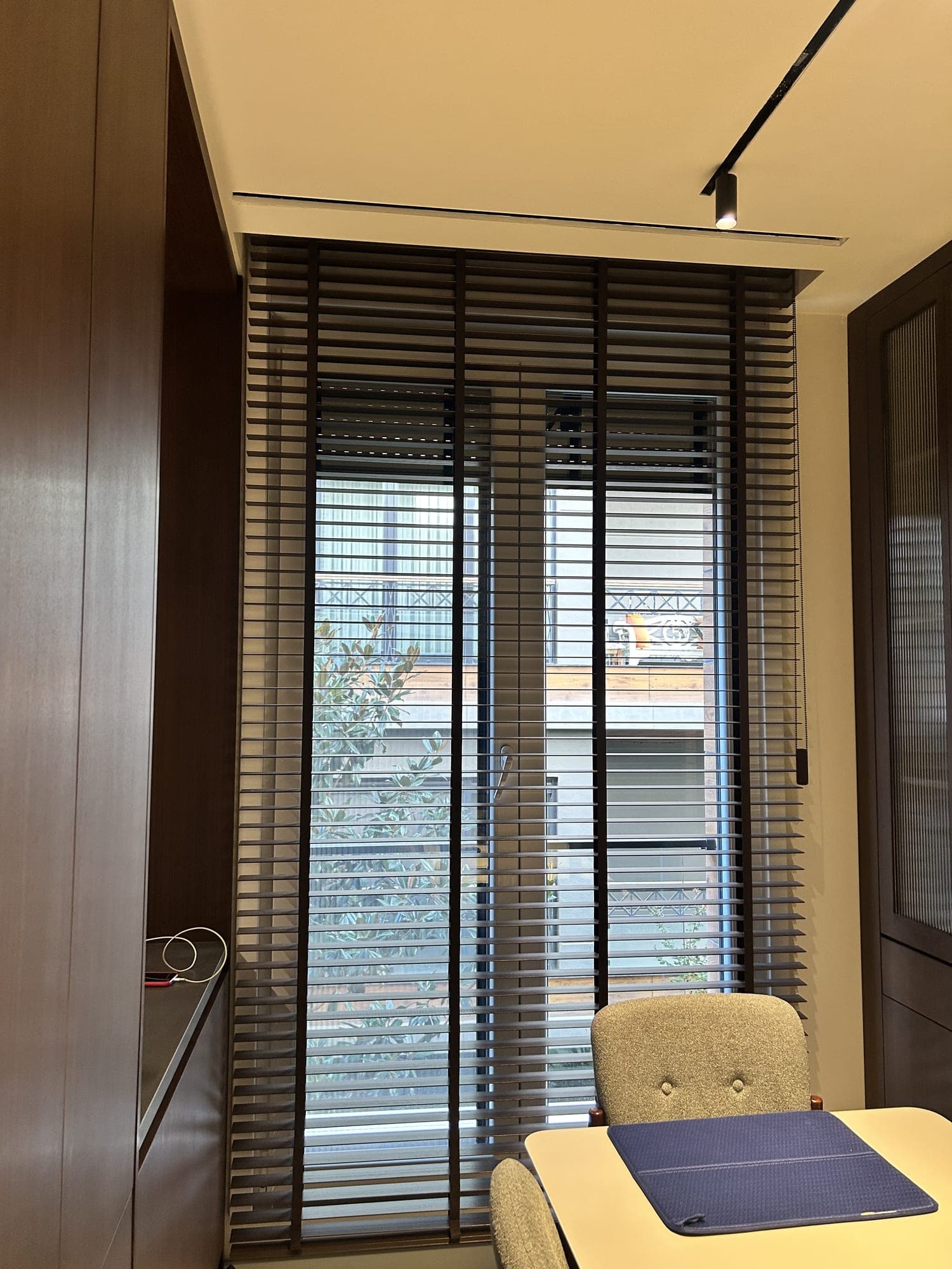 A wooden Venetian blind with fabric tapes falling from the ceiling between wooden cabinets in a study