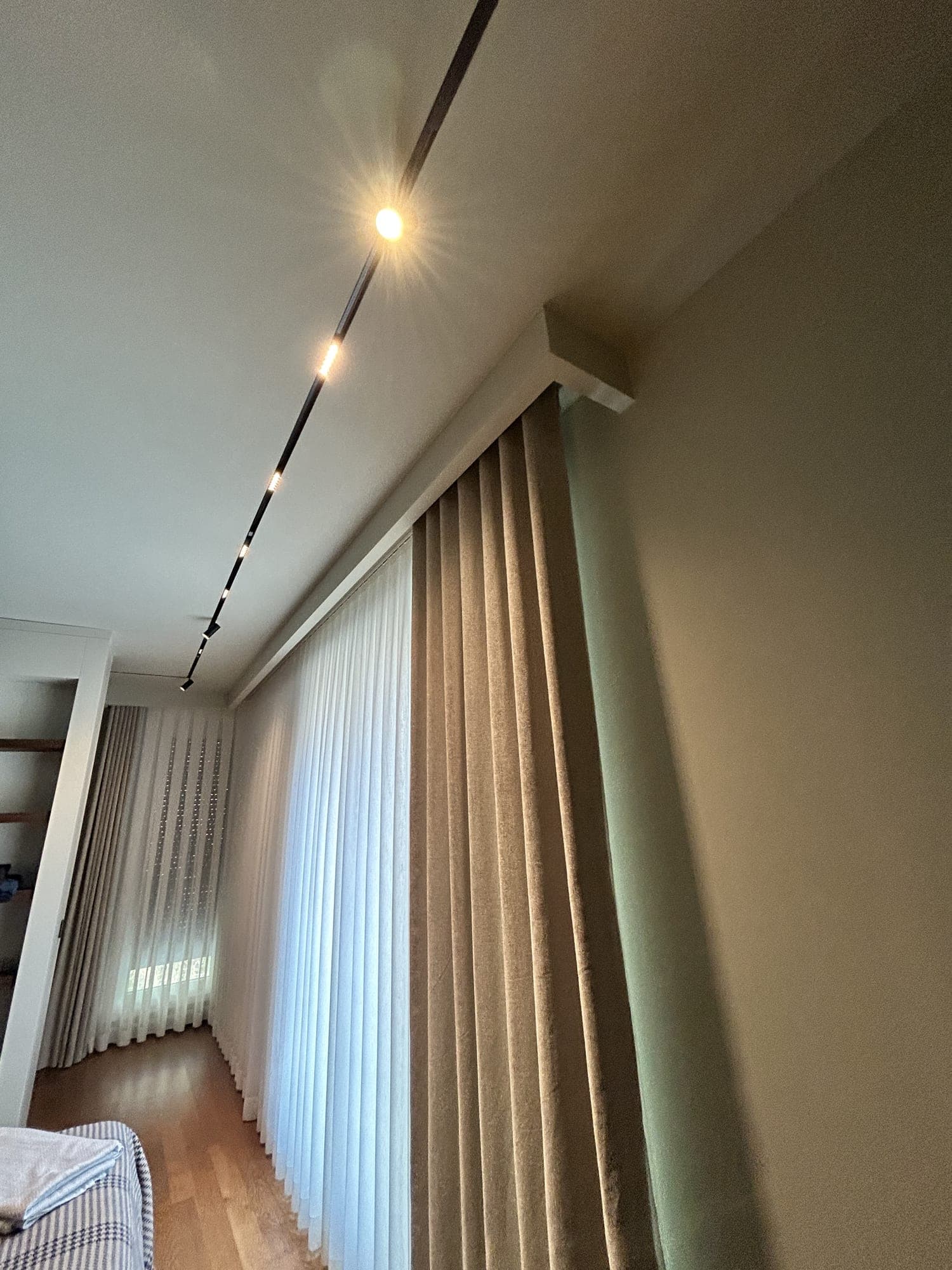 Sheer and drapes falling from a pelmet box that runs along a wall, in another room