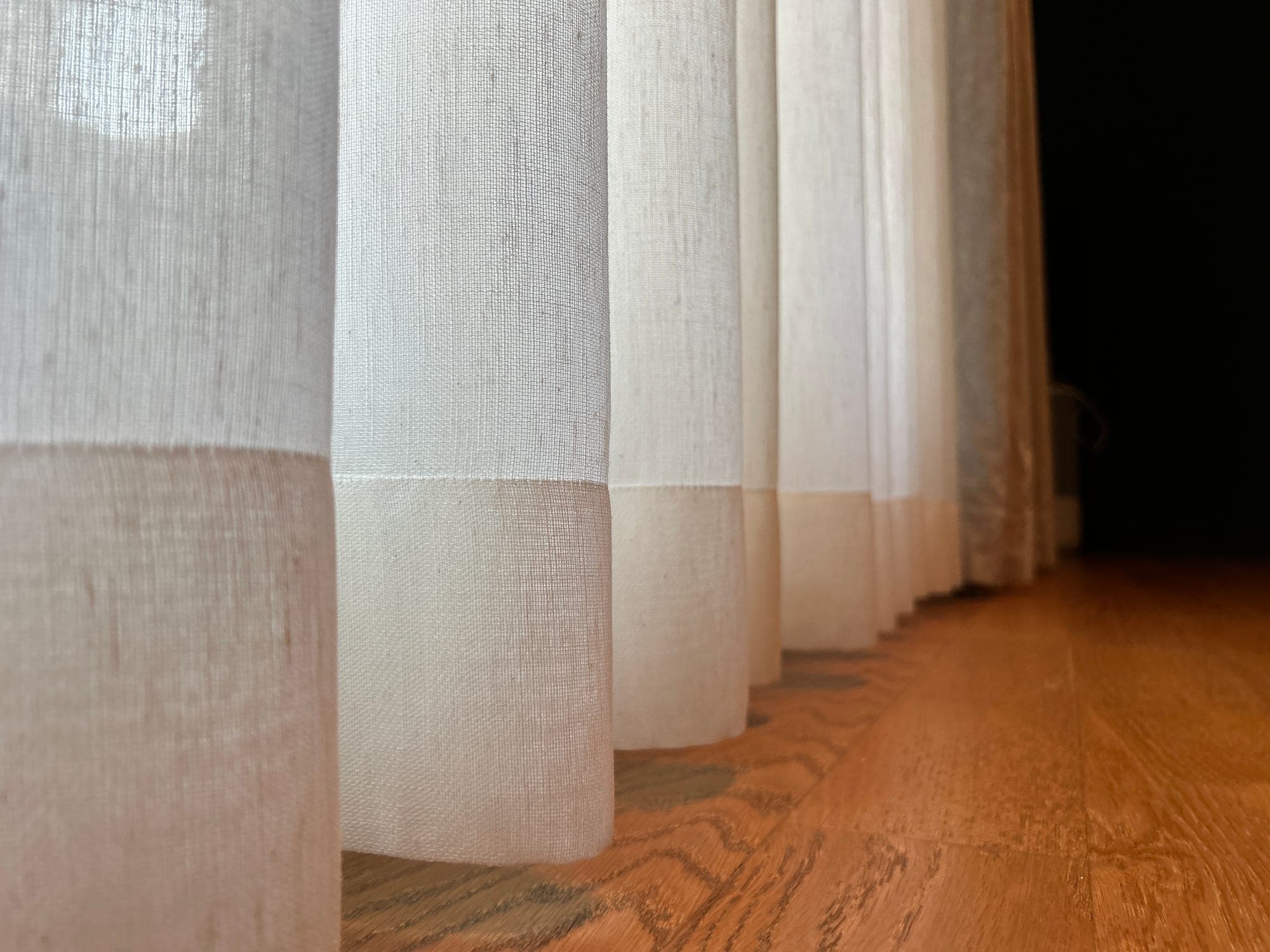 Hems of the linen-textured sheer, finished with a wide band, on a wooden floor