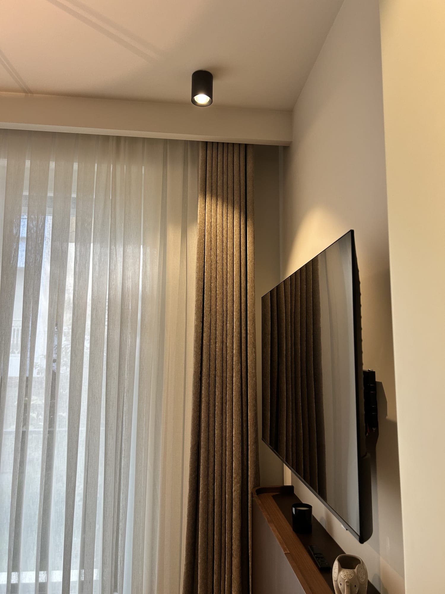 The corner where the drape meets the wall beside the window, under a ceiling spotlight