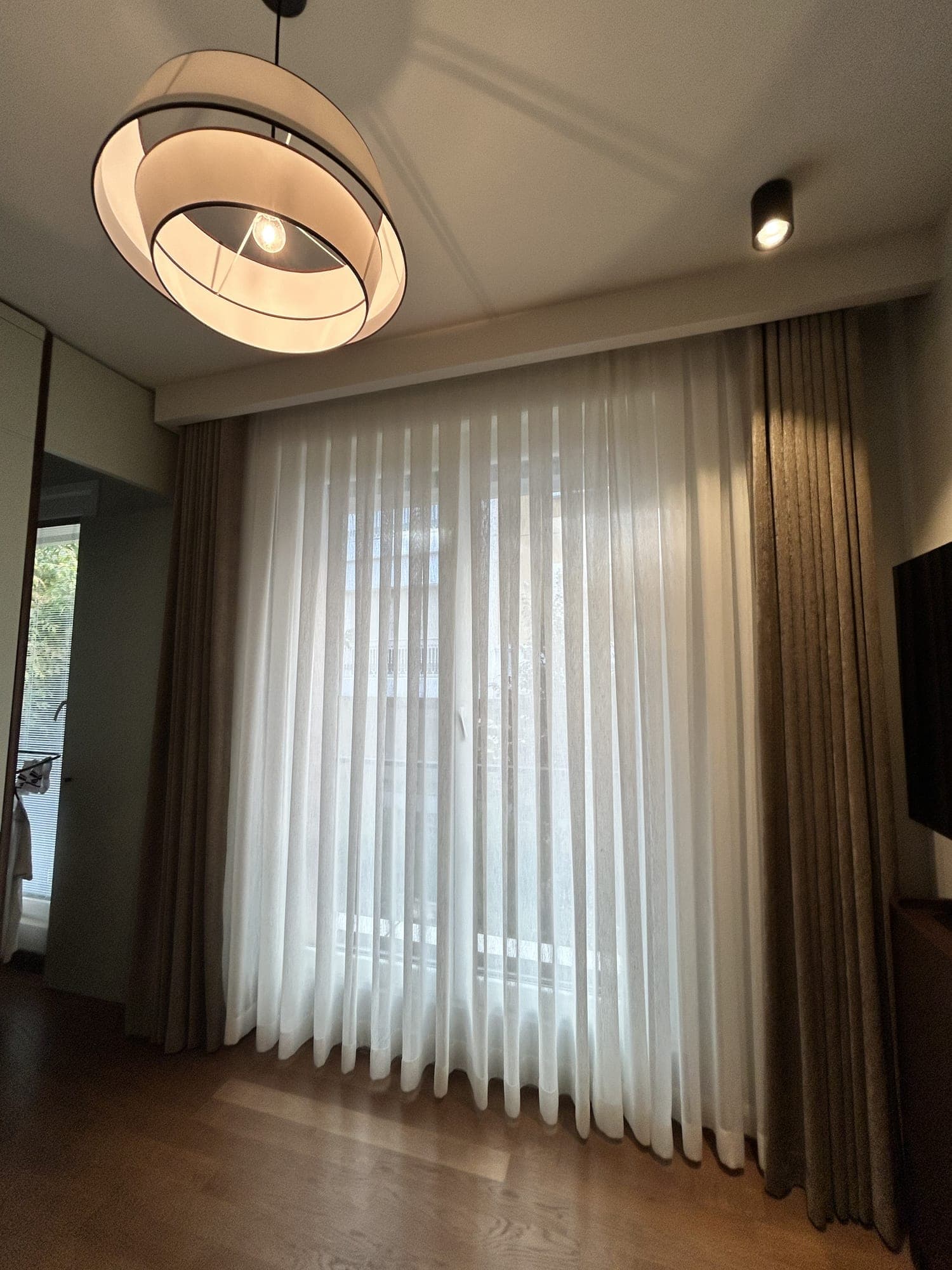 Floor-to-ceiling linen-textured sheer with earth-toned drapes on either side, in a room with a pendant lamp