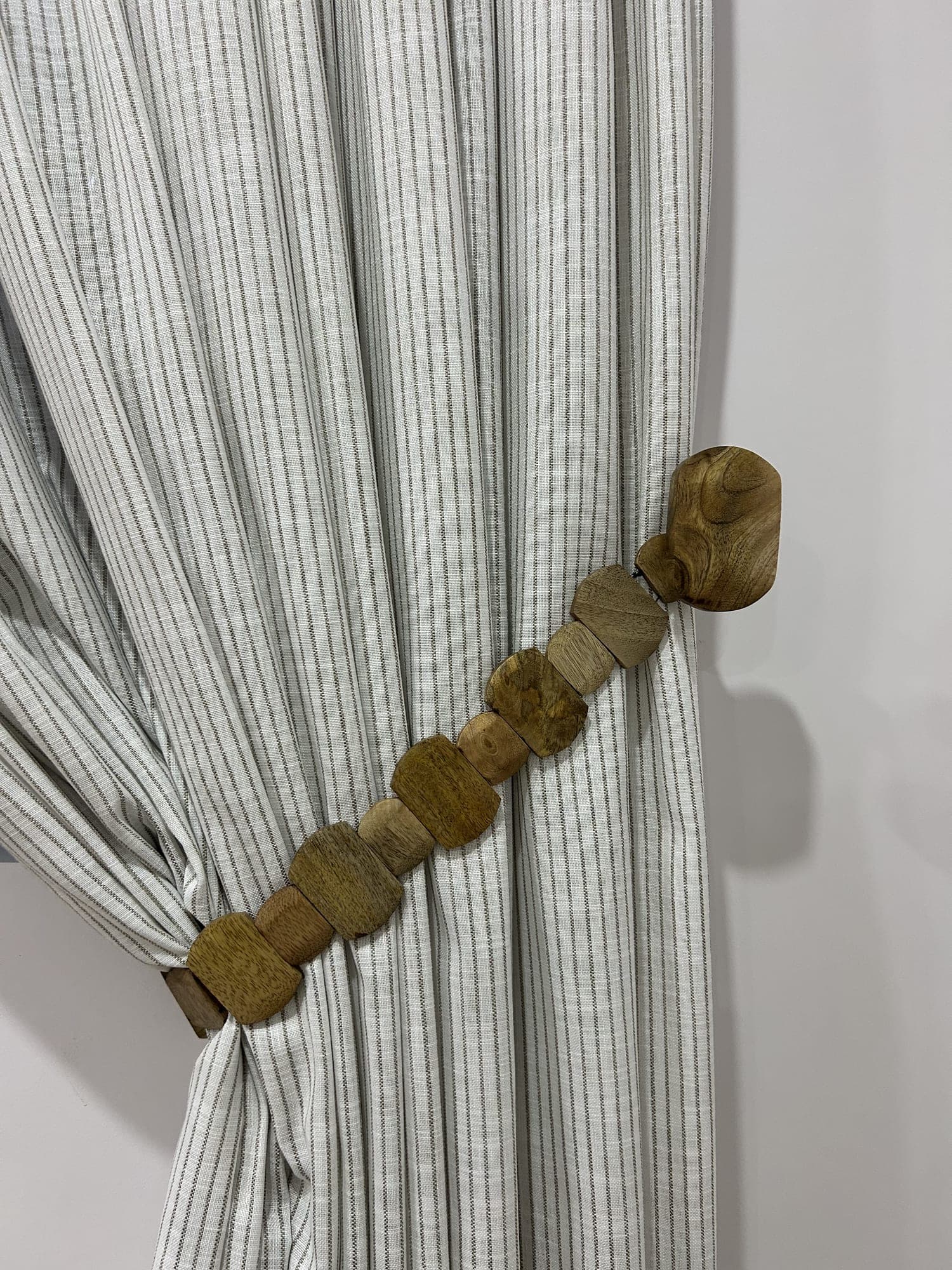 A striped drape gathered by a tieback of wooden beads, close up