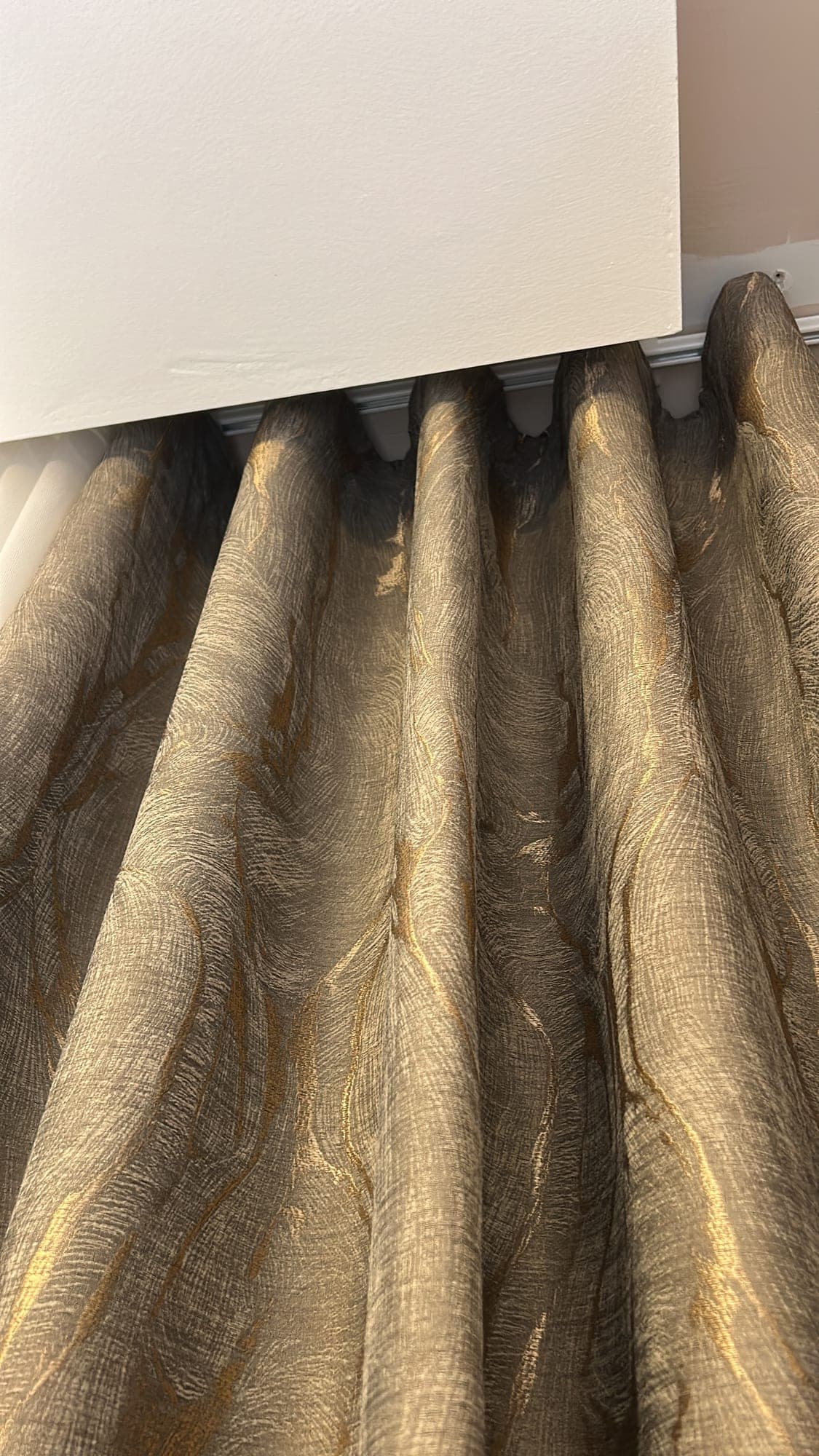 The wave heading of a textured drape with a gold sheen, close up