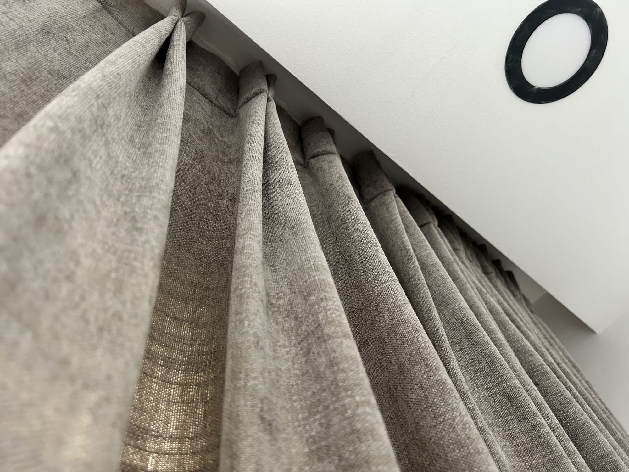 A grey drape falling in even waves from a track just under the ceiling, seen from below