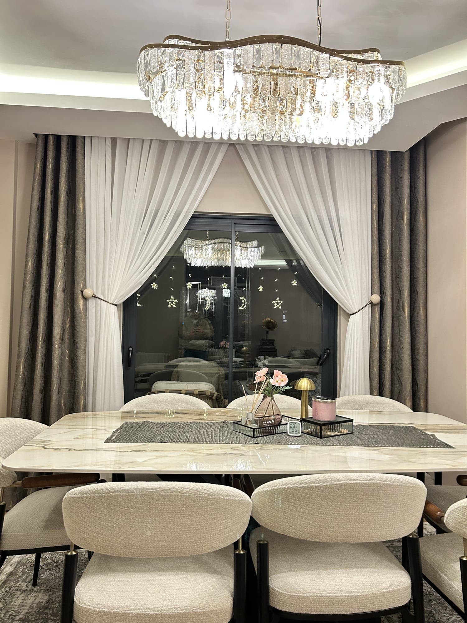 A dining room with a crystal chandelier: a sheer gathered to either side, with patterned drapes at both edges