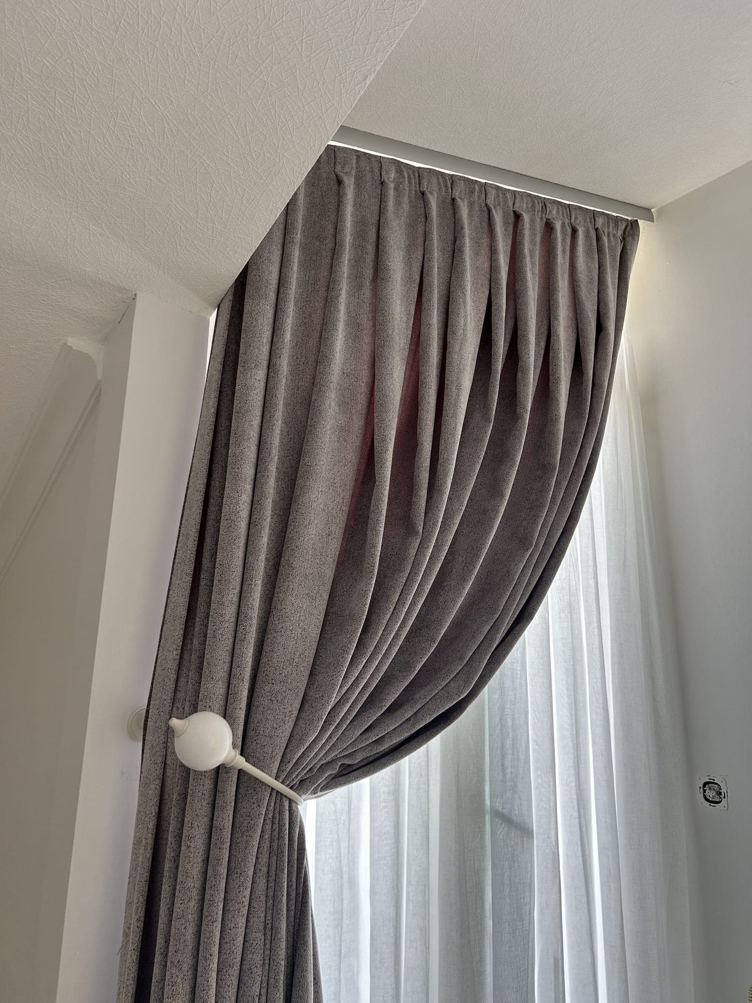A grey drape gathered to the side by a white holdback, a sheer behind