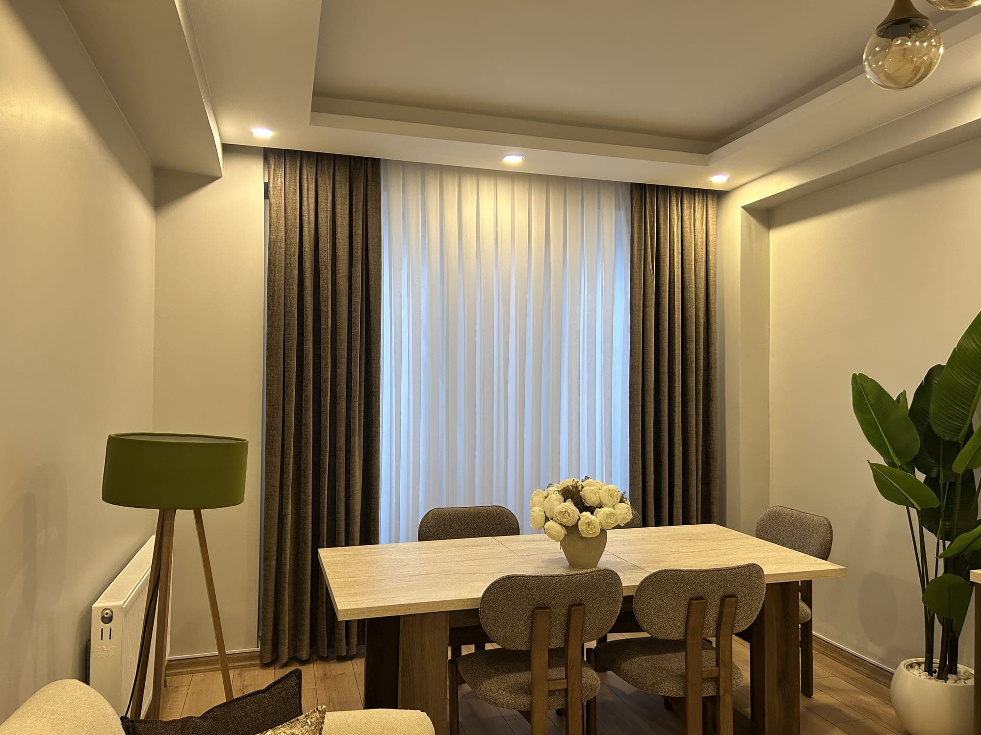Olive drapes on either side of a sheer in a dining room with a green lampshade